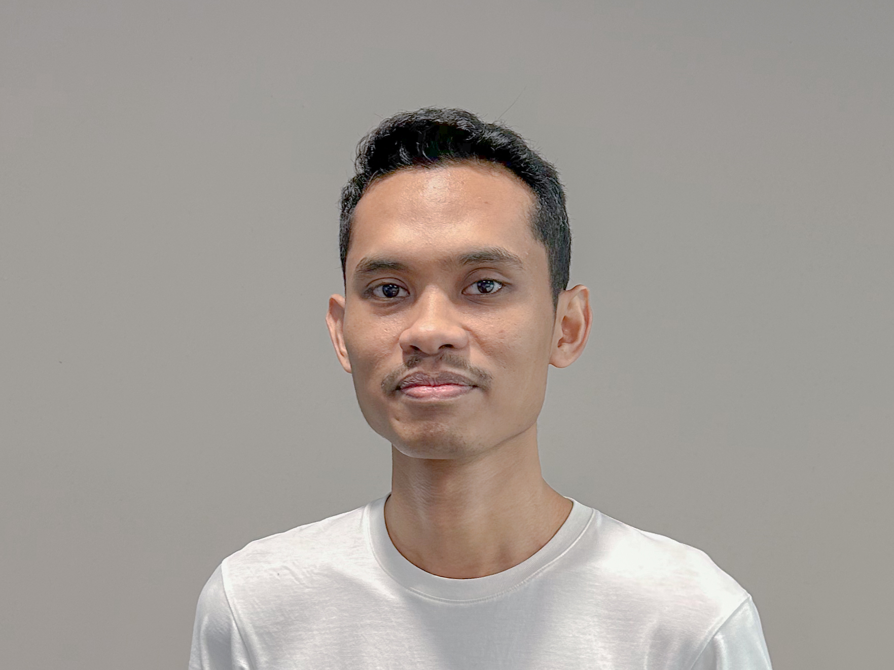 A portrait of me in a white t-shirt against a dark grey background.