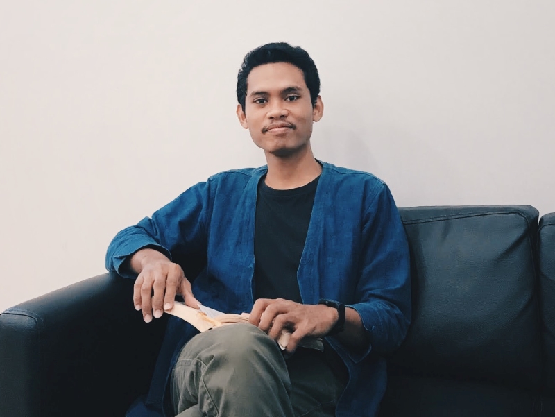 A photo of me wearing a blue outerwear and black t-shirt while holding an open book.